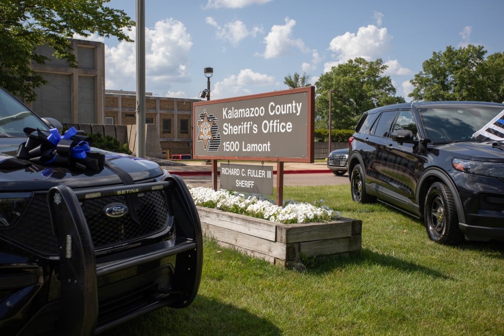 A sign stands between two sheriff's department vehicles. The sign reads "Kalamazoo County Sheriff's Office. Richard C. Fuller the third. Sheriff."