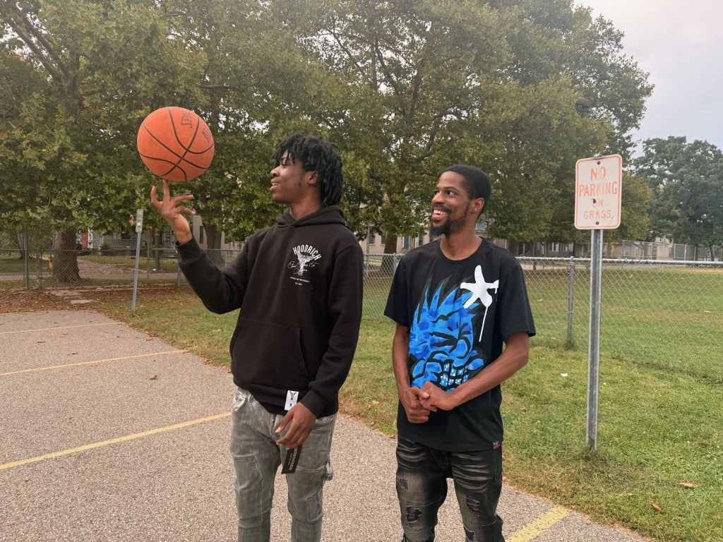 Dominic Deere smiles as his teenage son spins a basketball on his finger.