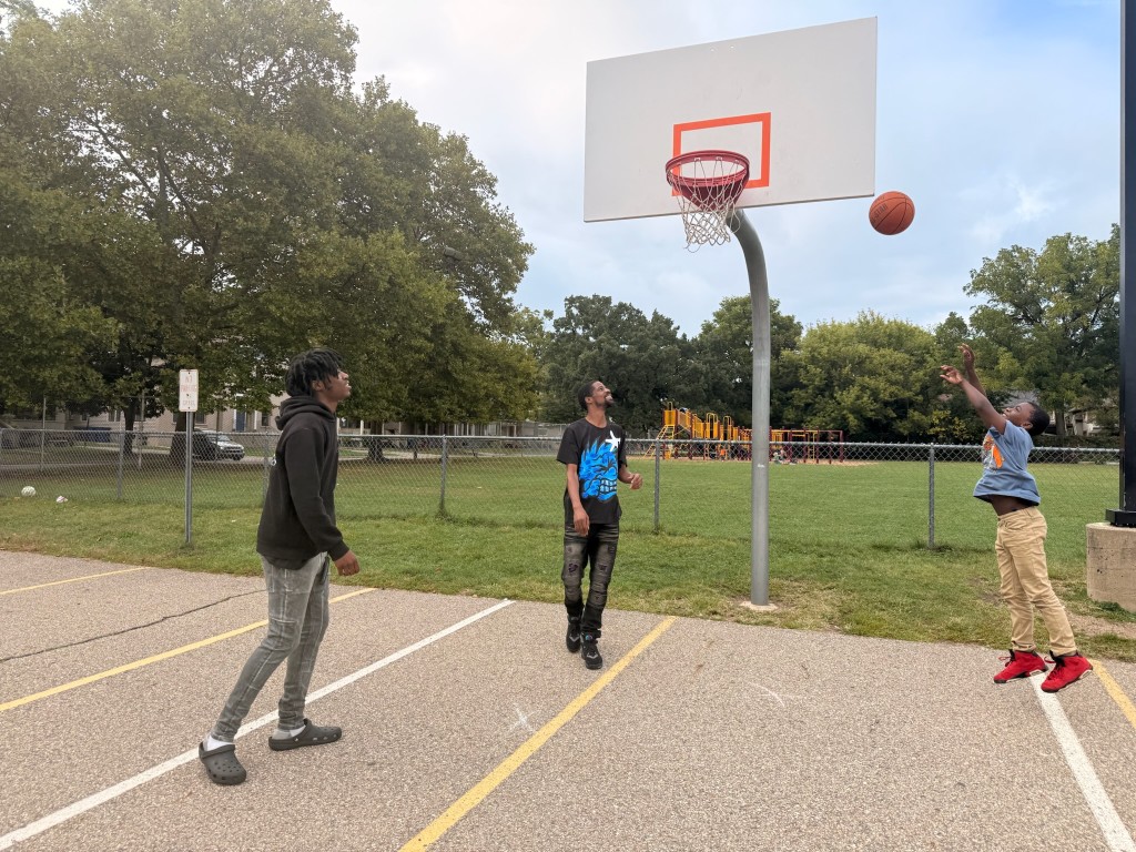 Dominic Deere watches as his young nephew jumps and throws a basketball toward a basketball hoop.