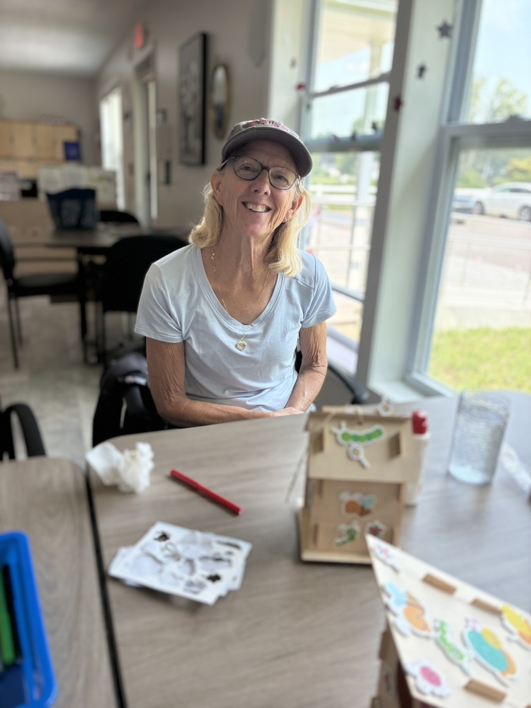 Nonprofit Spotlight: Wilbur and Charlotte Courter Memory Center 3 An older woman smiles next to a hand-decorated wooden birdhouse.