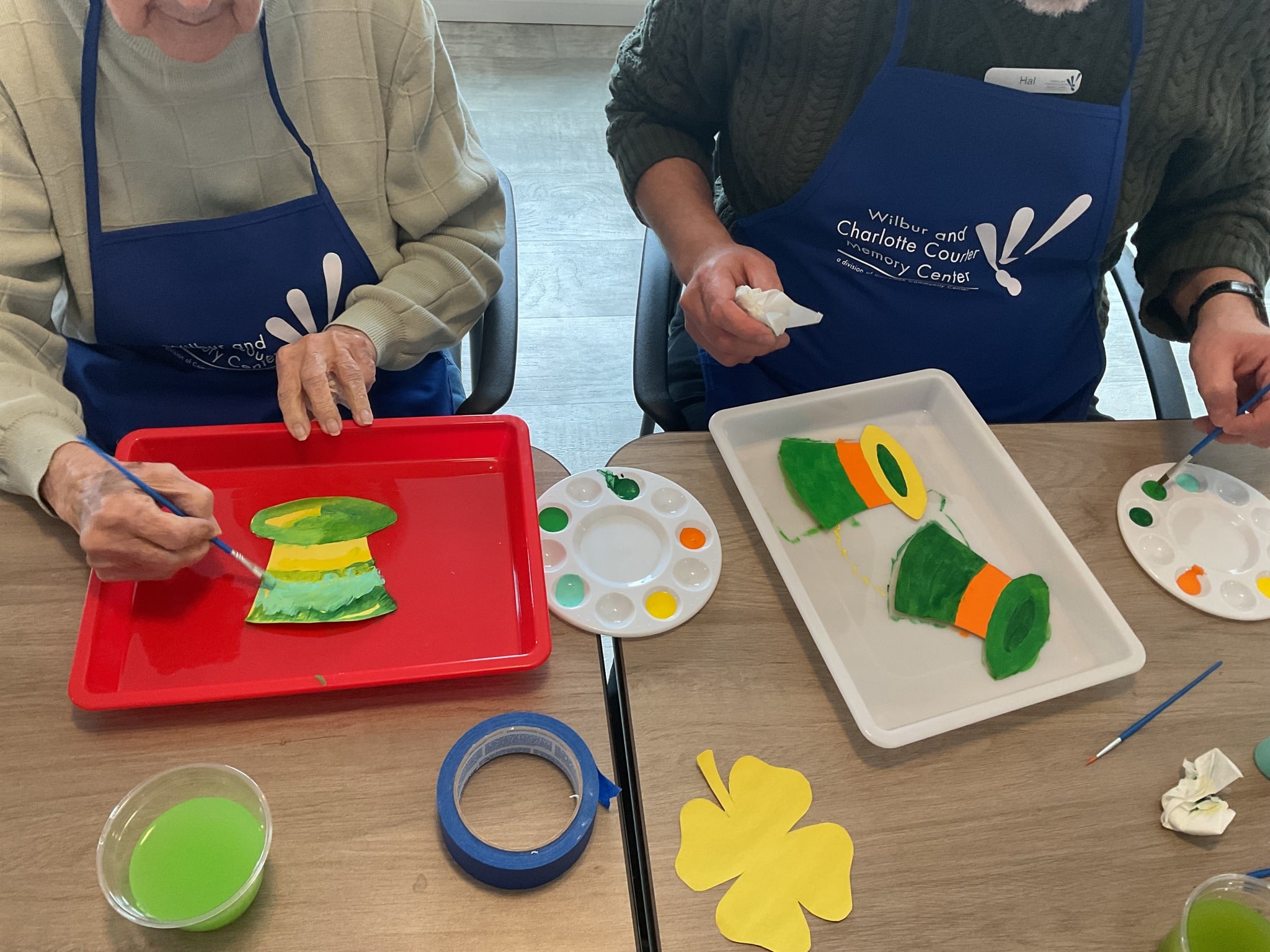 Nonprofit Spotlight: Wilbur and Charlotte Courter Memory Center 2 Two older people paint St. Patrick's Day crafts made to look like green top hats.